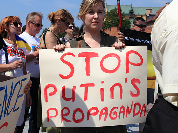 A photo of a protestor at a protest holding up a sign that reads "Stop Putin's Propaganda."