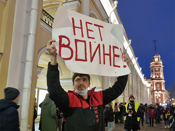 A photo of a protestor holding up a sign that reads "No War!" in Russian.
