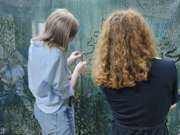 Photo of Emma Mateo learning how to sew camouflage netting from a volunteer in Dnipro. Leads to a postdoc spotlight