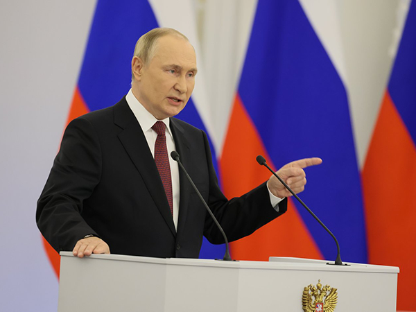Putin at a podium in front of Russian flags. Image links to event page.